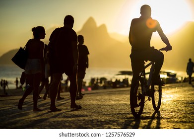 Scenic Sunset View Of Pedestrians And Cyclists Walking And Cycling On The Ipanema Beach Promenade In Rio De Janeiro, Brazil 