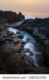 Scenic sunset view of rocky seashore with waves and misty water in twilight, long exposition. Dramatic and serene ocean landscape perfect for travel, nature, or coastal themes in photography.