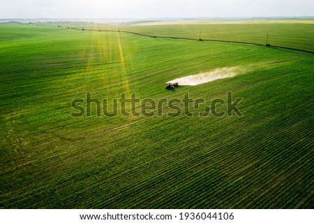 Scenic top view of a tractor spraying green fields. Organic irrigation field. Location place of Ukraine agrarian region, Europe. Aerial photography, drone shot. Industry of agronomy. Beauty of earth.