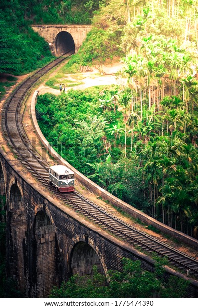 Scenic Train Ride over the world renowned demodara nine\
arches bridge. Service Car buggy train coming out of the ella\
tunnel in the morning light through beautiful lush green and tea\
estates. 