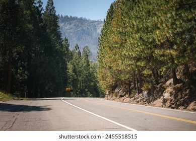 Scenic two lane road through forested area with no passing zone in Tahoe, California. Yellow road sign warns of left curve. Pine trees, mountains, clear sky.  - Powered by Shutterstock