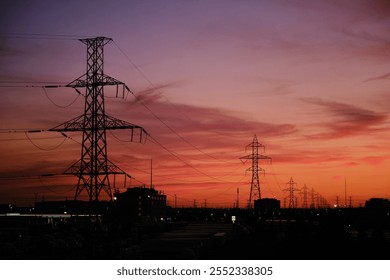 A scenic urban sunset featuring silhouetted power lines and a city skyline. The orange and purple sky creates a dramatic and serene atmosphere with industrial and natural elements in harmony. - Powered by Shutterstock