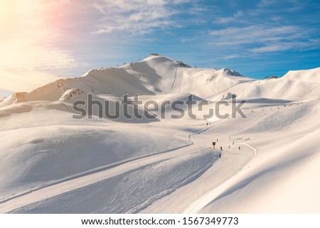 Scenic valley of hilghland alpine mountain winter resort on bright sunny day. Wintersport scene with people enjoy skiing and snowboarding on groomed pisets. panoramic wide view of downhill slopes