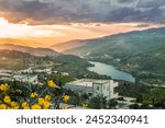 A scenic valley with a Water dam, green hills, and a sunset sky. A building stands amidst nature. It’s tranquil and picturesque.