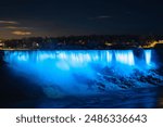 A scenic view of American Falls illuminated with lights in Niagara Falls in Ontario, Canada, at night