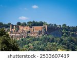 A scenic view of the ancient Roman fortress in Rome, Italy, surrounded by lush greenery under a clear blue sky.