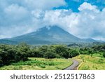 A scenic view of Arenal Volcano covered in clouds, with lush green fields and a winding road in the foreground, capturing the natural beauty and serenity of Costa Rica’s landscape.
