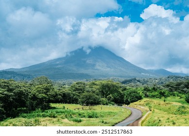 A scenic view of Arenal Volcano covered in clouds, with lush green fields and a winding road in the foreground, capturing the natural beauty and serenity of Costa Rica’s landscape.
 - Powered by Shutterstock