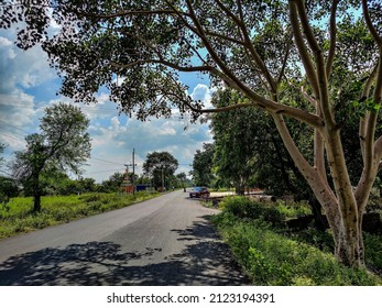 Scenic View Of Asphalt Road Connected To The Countryside Area, Big Trees Covered Road. Road Surrounded By Farmland , Small Hindu Temple Situated In The Farm. Car Moving Forward Under Bright Sunlight.