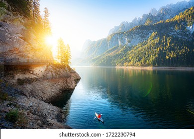 Scenic view of beautiful autumn scenery at famous alpine lake Gosausee with Dachstein mountain summit and young adventurist kayaking in golden morning light at sunrise in fall, Salzkammergut, Austria - Powered by Shutterstock