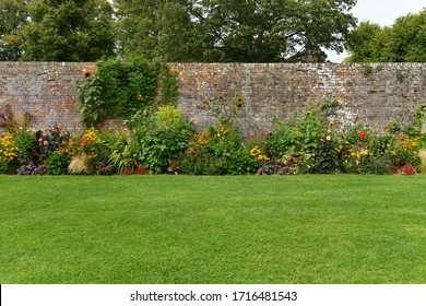 Ein wunderschöner Ausblick auf einen schönen Landschaftsgarten im englischen Stil mit grünem Rasen, farbenfrohen Blumenbeeten und gedeckter Mauer aus Redzick