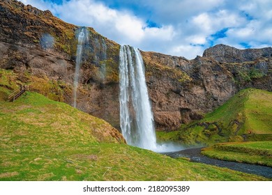 Scenic view of beautiful Seljalandsfoss flowing from mountain. Majestic powerful waterfall against cloudy sky. Picturesque view of famous attraction in valley.