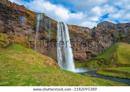 Scenic view of beautiful Seljalandsfoss flowing from mountain. Majestic powerful waterfall against cloudy sky. Picturesque view of famous attraction in valley.