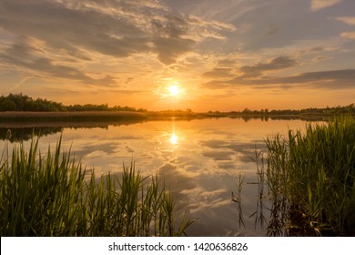 Scenic view of beautiful sunset or sunrise above the pond or lake at spring or early summer evening with cloudy sky background and reed grass at foreground. Landscape. Water reflection. - Shutterstock ID 1420636826