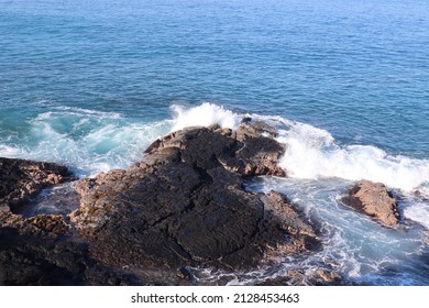 A Scenic View Of Black Volcanic Rock On The Ocean Water's Edge In Kona, Hawaii