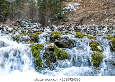 A scenic view of a cascading stream flowing over moss-covered rocks in a forest setting. The clear, rushing water and vibrant greenery create a refreshing and peaceful atmosphere perfect for nature  - Powered by Shutterstock