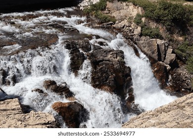 A scenic view of a cascading waterfall flowing over rocky terrain surrounded by lush greenery. - Powered by Shutterstock