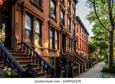 Scenic view of a classic Brooklyn brownstone block with a long facade and ornate stoop balustrades on a summer day in Clinton Hills, Brooklyn