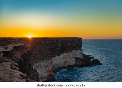 A scenic view of the cliffs at Nullarbor during sunset, showcasing the vibrant colors of the sky and the ocean waves crashing against the rocks