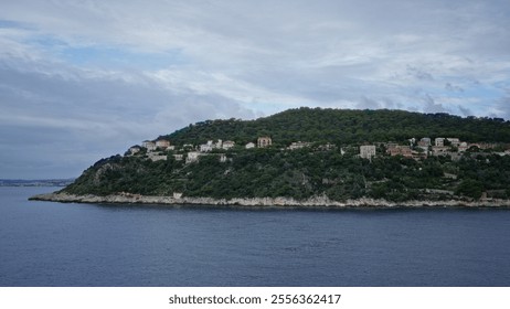 Scenic view of coastal hillside with lush greenery and houses overlooking calm sea under cloudy sky. - Powered by Shutterstock