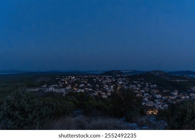 Scenic view of coastal village illuminated at twilight, surrounded by hills and sea under deep blue evening sky. Concept of serene landscapes, peaceful living, and natural beauty. High quality photo - Powered by Shutterstock