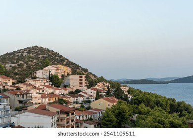 Scenic view of coastal village nestled against hillside with Mediterranean architecture overlooking calm sea on tranquil evening. Mediterranean charm, and coastal landscapes. . High quality photo - Powered by Shutterstock