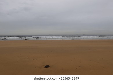 Scenic view of a deserted beach meeting the wavy ocean under a cloudy sky, creating a serene and melancholic atmosphere - Powered by Shutterstock