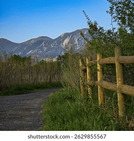 A scenic view of a dirt path bordered by a wooden fence, leading towards a backdrop of mountains under a clear sky. - Powered by Shutterstock - Get 15% off with code: PIKWIZARD15