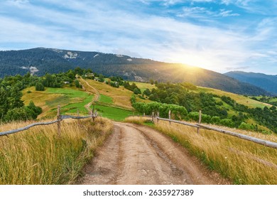 Scenic view of a dirt path running alongside a wooden fence on a high, grassy mountain slope. Layered forested hills visible under a clear blue sky. Hiking trail. - Powered by Shutterstock - Get 15% off with code: PIKWIZARD15