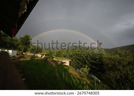 Scenic view of a double rainbow spanning over forested landscape and small houses