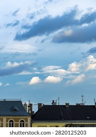 Scenic view of dramatic clouds above historic European city rooftops at golden hour. Urban skyline with old architecture under a colorful evening sky. Travel and cityscape concept.