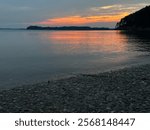 Scenic view from the edge of a rocky area on Lake Ouachita in Arkansas, as the sun sets, casting a warm glow over the water and surrounding landscape