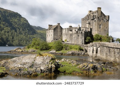 Scenic view of Eilean Donan Castle by Loch Duich, surrounded by lush greenery and a calm lake - Powered by Shutterstock