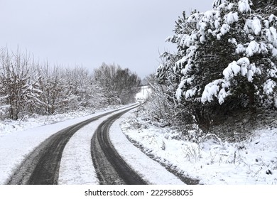  Scenic view of empty, not cleared road with snowy landscape during snowfall in winter season. Right turn onto a slippery winter road. A gloomy winter day. Ukraine.