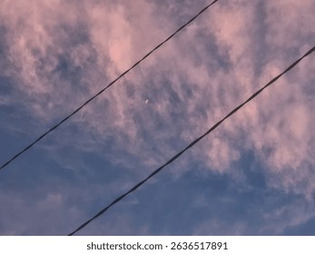 A scenic view of the evening sky with soft pink clouds and a crescent moon, intersected by two power lines running diagonally across the frame - Powered by Shutterstock - Get 15% off with code: PIKWIZARD15