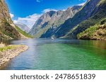 A scenic view of a fjord with a boat sailing in the water surrounded by mountains and a clear blue sky in Norway