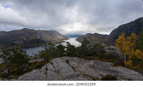 A scenic view of a fjord surrounded by rocky hills and sparse trees under a cloudy sky. - Powered by Shutterstock