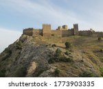 Scenic view of the Fortress mountain, covered with shrubs and faded grass in the sun and an ancient fortress with a defensive wall and towers on a warm summer evening. Genoese fortress, Sudak, Crimea