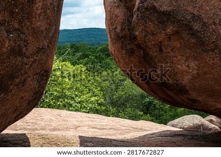 A scenic view framed by massive granite boulders overlooking a lush forest and rolling hills, showcasing the natural beauty of a rocky landscape.