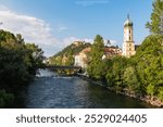 Scenic view of Franciscan Church in old town of Graz, Styria, Austria, Europe. Uhrturm Clock Tower on Schlossberg in background. Mur river flowing through city. Charming cityscape with red-tiled roofs