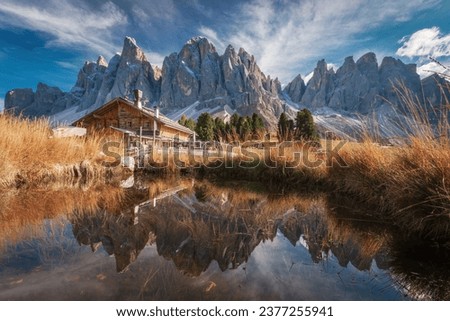 Scenic view of Geisler Alm Rifugio delle Odle in front of dolomites mountains and reflection in the water of a pond, South Tyrol, Italy