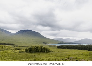 A scenic view of Glencoe Valley featuring lush greenery, distant mountains, a lake, and an overcast sky - Powered by Shutterstock