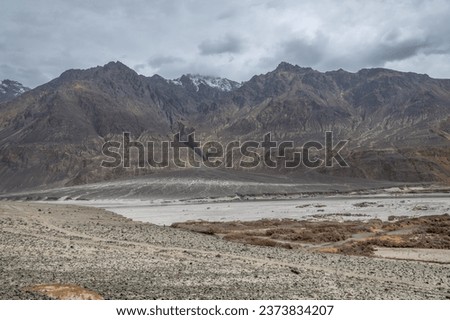 Scenic View of high peaks of Himalaya with river flowing in the foot of the hills Dry river in summer, riverside vegetation, and rocky terrain The cold desert of Ladakh in India