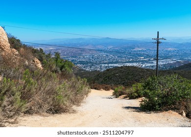 Scenic view from hillside dirt trail at Cowles Mountain in Mission Trails Regional Park, featuring a dirt path, power lines, and distant suburban sprawl - Powered by Shutterstock