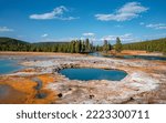 Scenic view of hotspring by Firehole River in Midway Geyser Basin. Water flowing by geothermal landscape with sky in background at famous Yellowstone national park. Sightseeing attraction in summer.