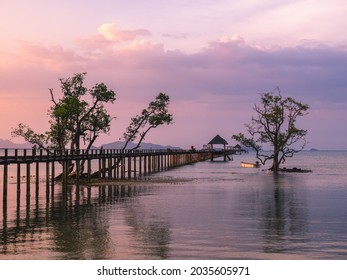 Scenic view of infinity long wooden pier boardwalk and tree over peaceful bay of water with reflection in sunset orange cloud sky. Landmark of Koh Mak Island, Trat, Thailand. Wide angle background.