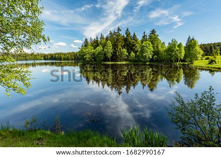 Scenic view of a Kladska lake in the Czech Republic, close to Marianske Lazne surrounded with forest. Sunny summer landscape with blue sky and white clouds and reflection in water.
