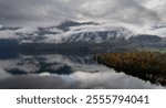 Scenic view of lake bohinj with colorful autumn forest and low clouds covering mountain on a cloudy day