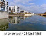 Scenic view of lake with reed and modern apartment buildings with blue cloudy sky on an autumn day at Swiss town of Opfikon Glattbrugg. Photo taken November 8th, 2024, Zurich Opfikon, Switzerland.