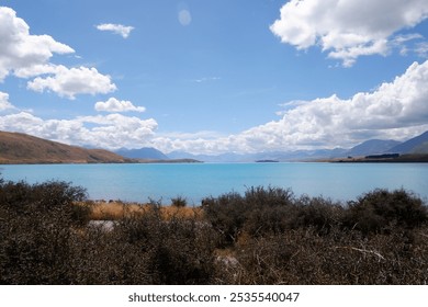 Scenic View of Lake Tekapo with Vibrant Blue Water on a Sunny Summer Day, Surrounded by Rocky Shoreline and Golden Grass under Clear Blue Sky – South Island, New Zealand - Powered by Shutterstock